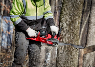 Workman in hi-vis coat and protective pants using a Milwaukee chainsaw on a tree