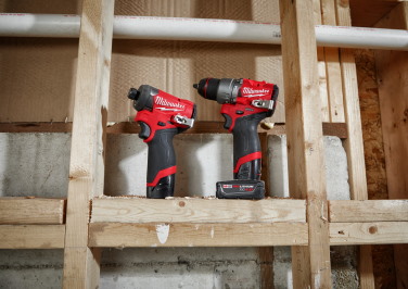 Two Milwaukee M12 drill-drivers resting on wooden frame of a room under construction