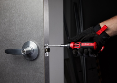 A gloved hand uses a screwdriver to tighten the screws on a brand new doorknob attached to a door