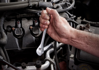 A mechanic's hand uses a wrench to tighten a bolt on the engine block of an automobile
