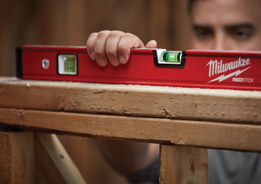 A contractor uses a Milwaukee level to true up a window frame while framing a house 