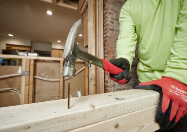 Workman in a hi-vis shirt and Milwaukee work gloves uses a Milwaukee hammer to pound nails