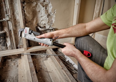 Workman uses a pipe wrench to bend a tube around the frame of a room he is building.