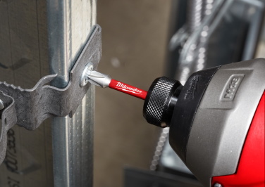 A Milwaukee power driver drives a screw into a bracket on a steel building frame.