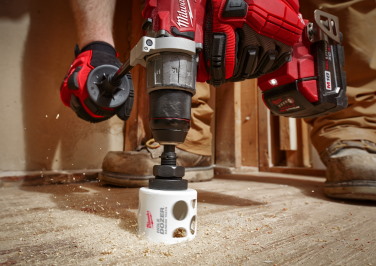 Workman uses a Milwaukee hole saw to cut a 3" hole in a floor system.