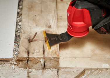 A Milwaukee multi-tool cuts exposed nails off of a 2x4 on a jobsite.