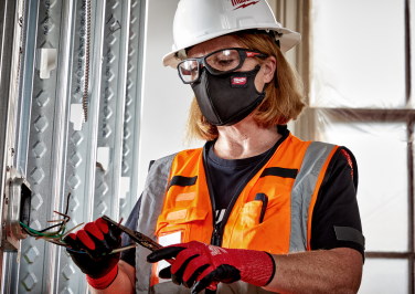 A female electrician strips wires while wearing Milwaukee protective gloves and equipment on the job